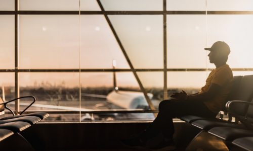 A man sitting by large windows at the airport with a sunset background