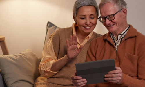 Two elderly people sitting on a couch and browsing on a tablet