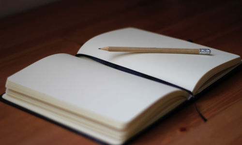 An empty journal laying open with a pencil resting on it. 