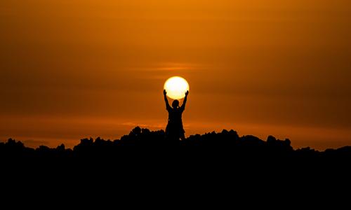 Person standing in the sunset holding up the sun. 