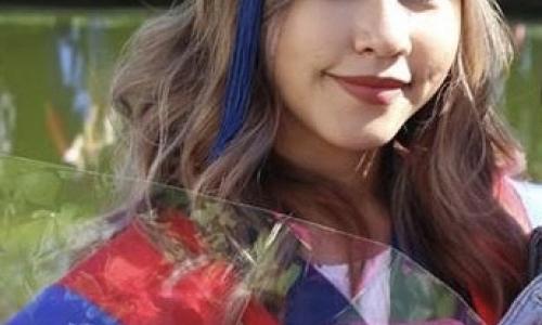 Image of Nikki in convocation cap and gown holding flowers at her Ugrad Communication Convocation
