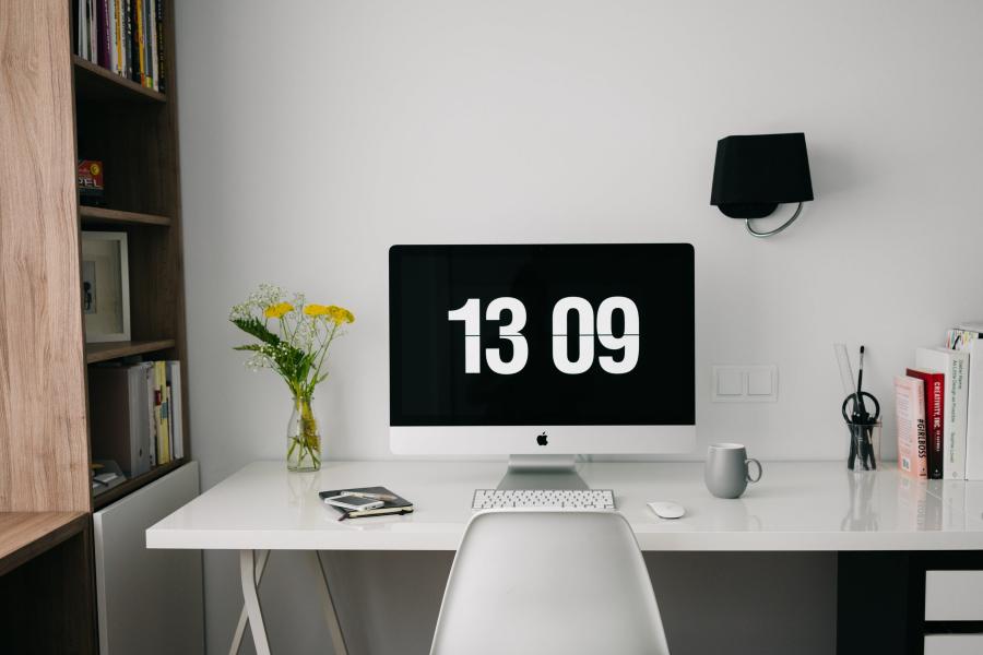 time (13:09) showing on a computer screen, placed on a table filled with office paraphernalia 