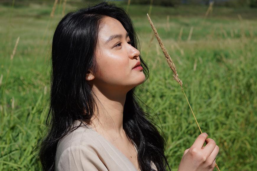 Close up of Linh's side profile while she is sitting in a field, looking into a distance