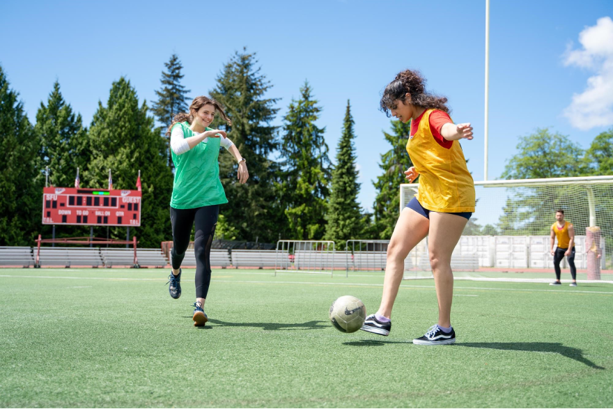 Two girls kicking around a soccer ball on a soccer field. 