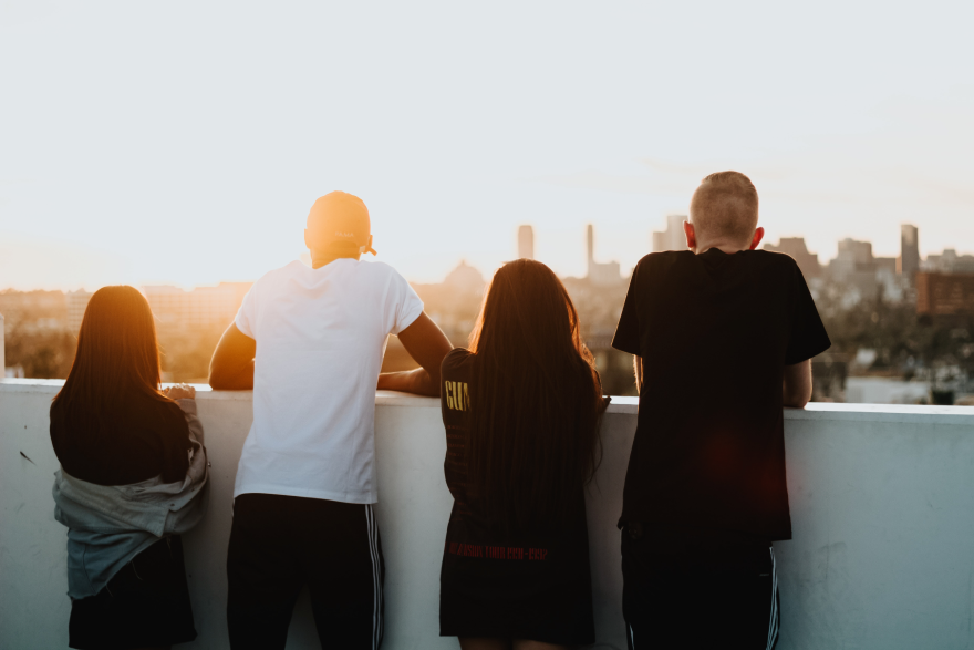 Four people looking at a sunset against a city