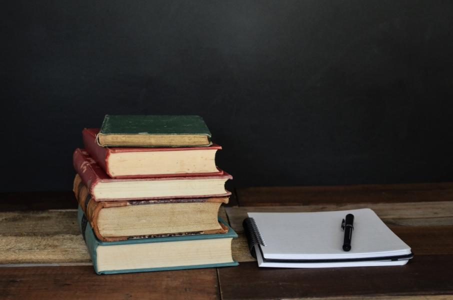 A stack of books and a notebook on a desk