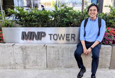 man sitting outside in front of sign that says "mnp tower"