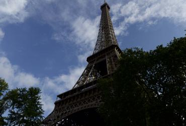 Photo of the Eiffel Tower taken from below. The sky behind is blue with white clouds.