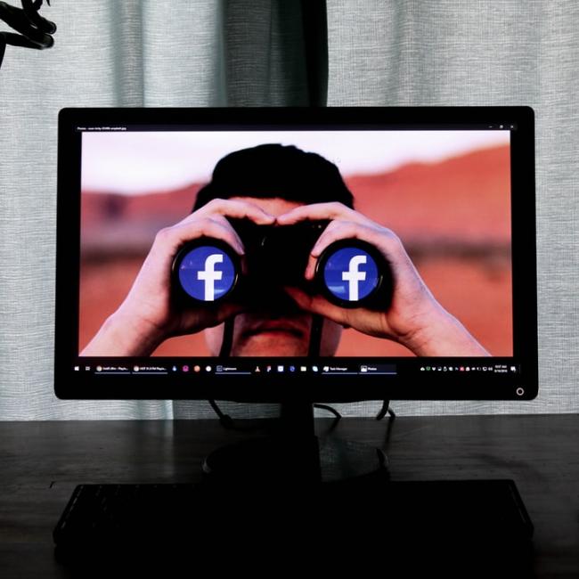 a computer screen showcasing a man holding binoculars with Facebook icons as the lens