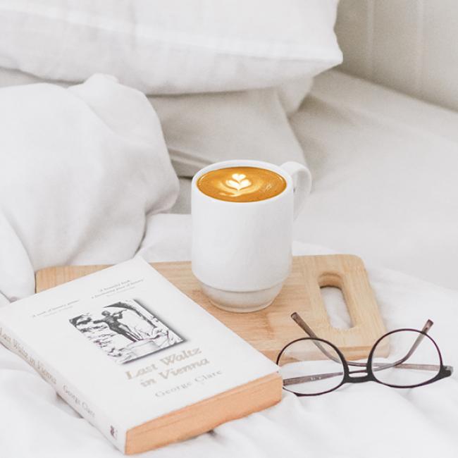 a bed spread containing coffee mug, glasses, and a book