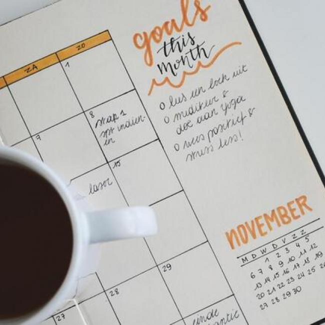 A cup of coffee placed on a written planner with the word "goals" next to it