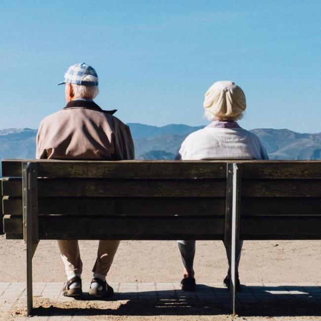 Older couple sitting on bench, looking out at mountain and ocean views