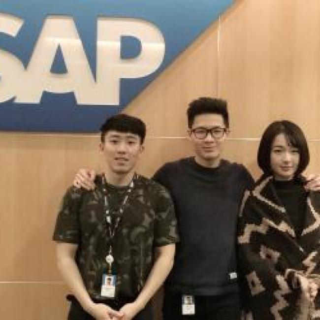 Three people posing in front of the SAP logo 