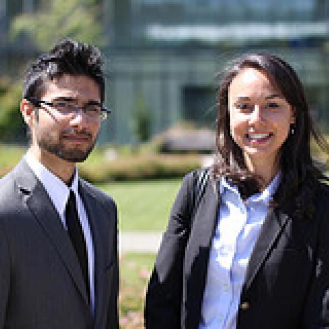 A man and a woman in a business suit are smiling while facing the front. 
