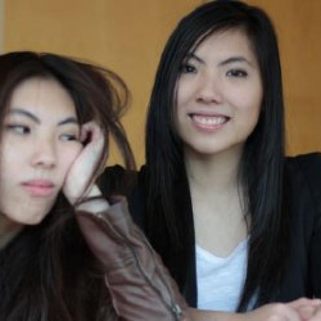 two girls sitting side-by-side, one frowning and the other smiling