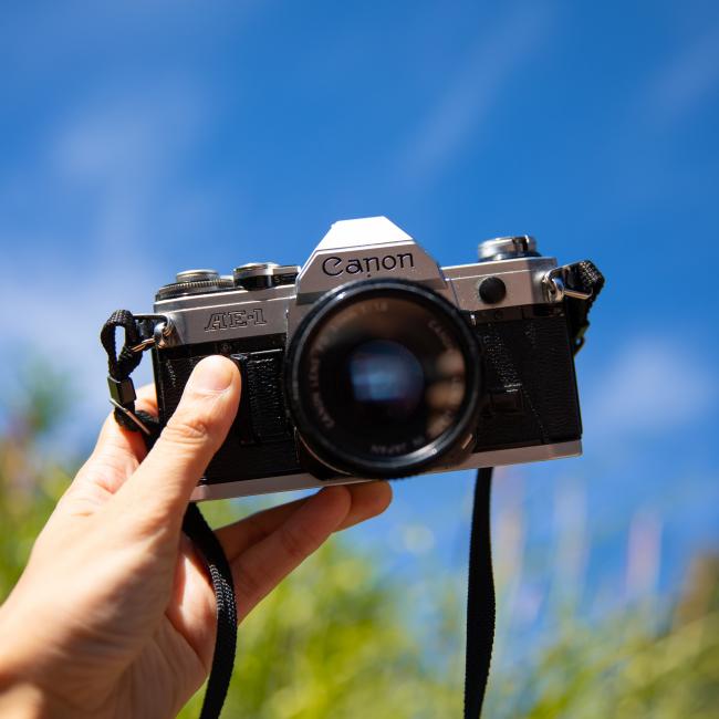 A hand holding a camera in front of a blue sky. 