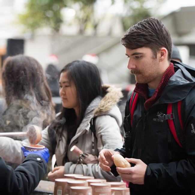 A person serving soup to people in line. 