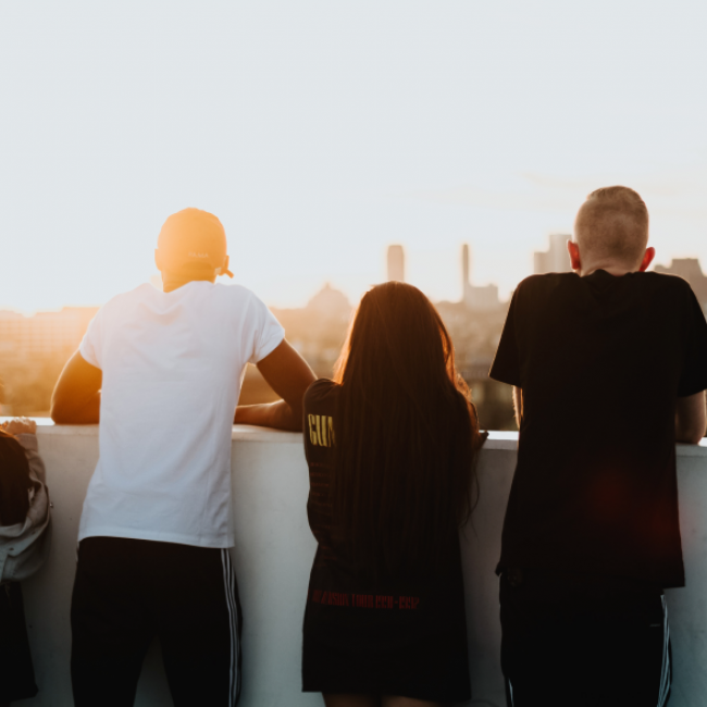 Four people looking at a sunset against a city