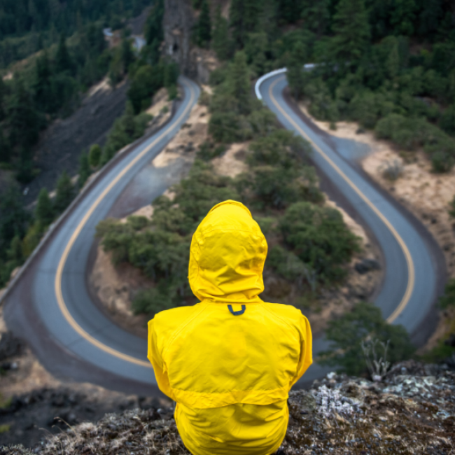 Person wearing a raincoat sitting above an empty road 
