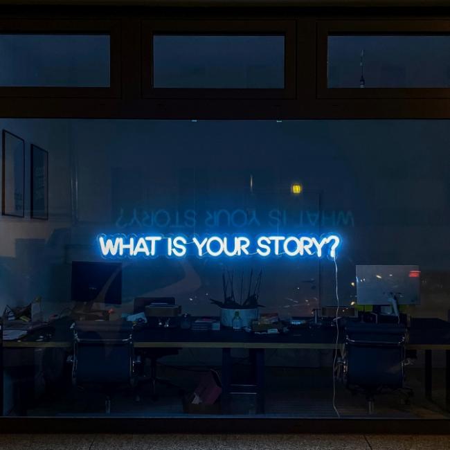 Neon lights on a window reading "What is your story?"