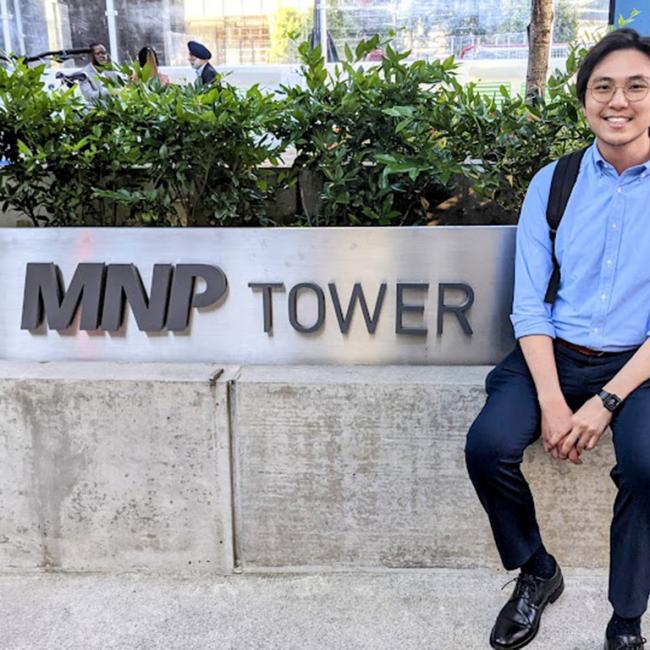 man sitting outside in front of sign that says "mnp tower"