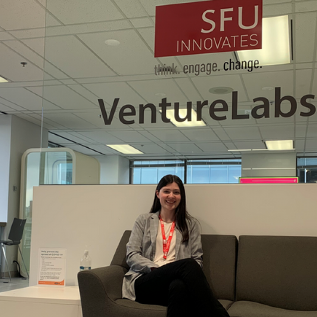 Amy sitting on a sofa, with the SFU VentureLabs logo behind her