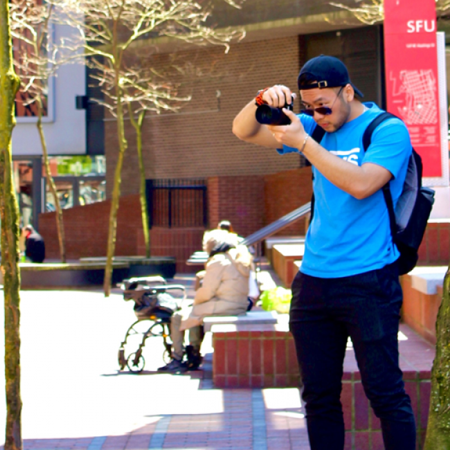 Elvis standing in front of Simon Fraser University holding a camera