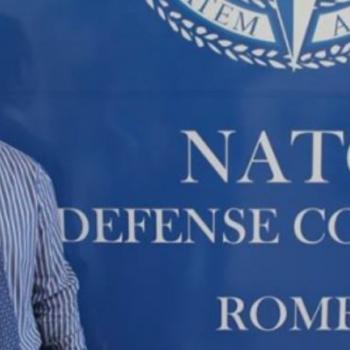 Cornel standing in front of a NATO Banner